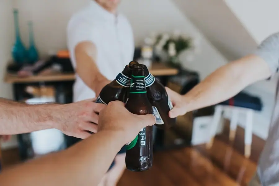 Hands clinking dark beer bottles together during wedding preparations.