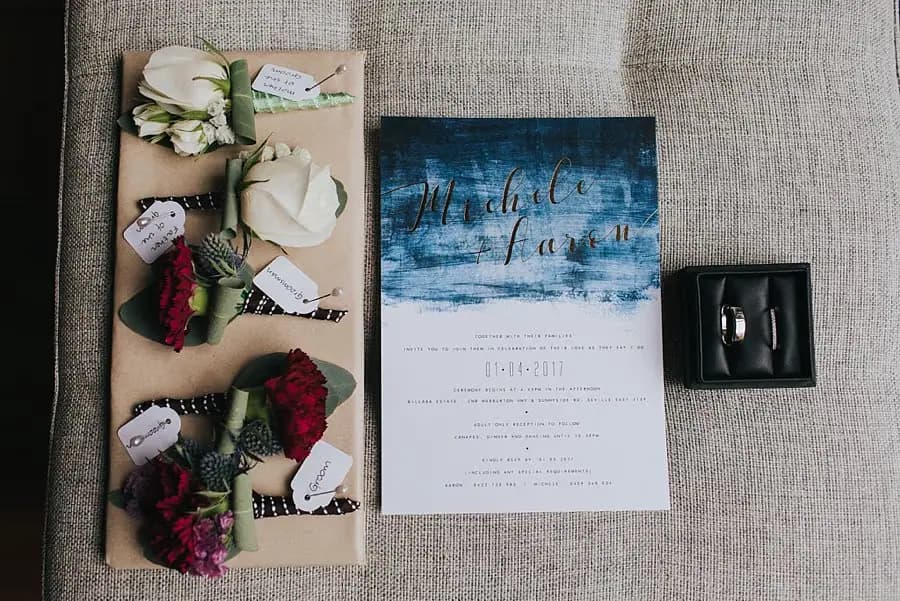 Wedding invitation, flower buttonholes and a small black box arranged on a sofa.