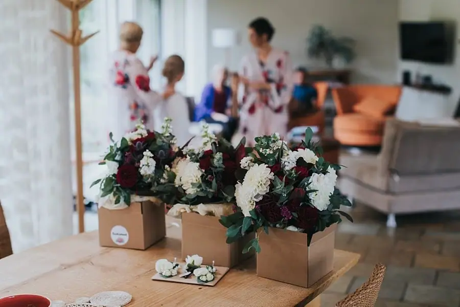 Red and white bouquets in boxes on a table while people prepare behind them.