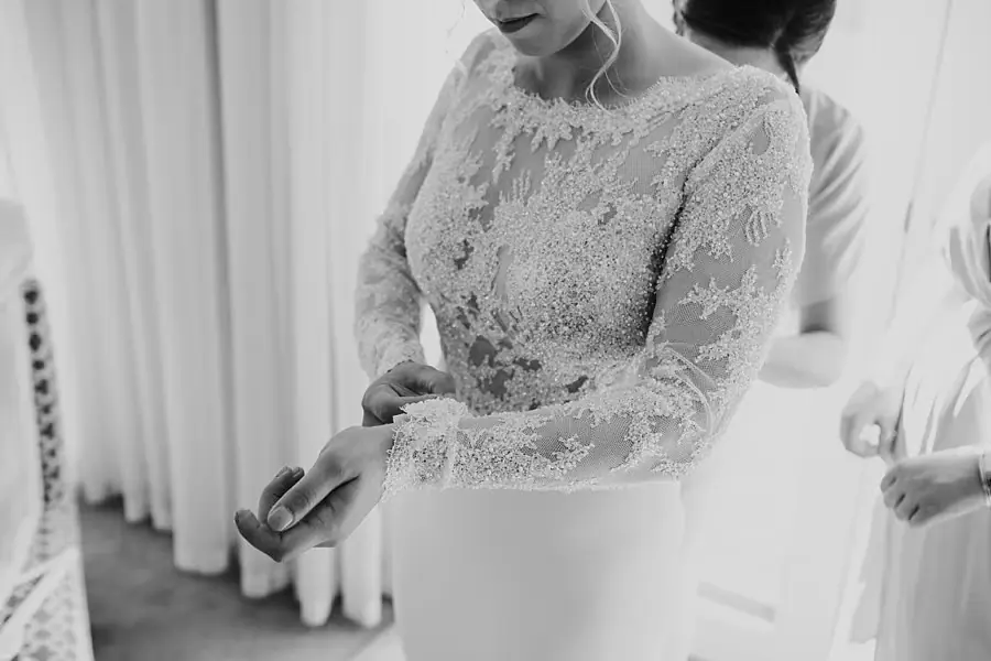 Black-and-white close-up of the bride adjusting her lace sleeve.
