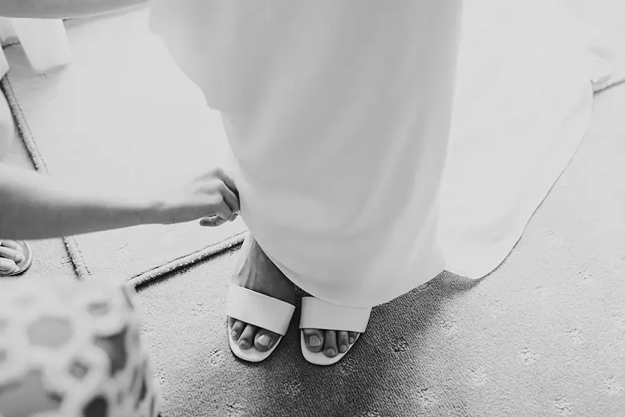 Black-and-white close-up of the bride's pale open-toe shoes beneath her dress.