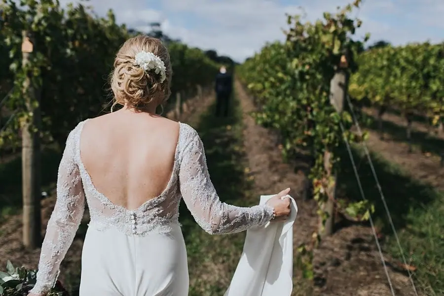 Bride approaching through the vineyard while lifting the skirt of her dress.