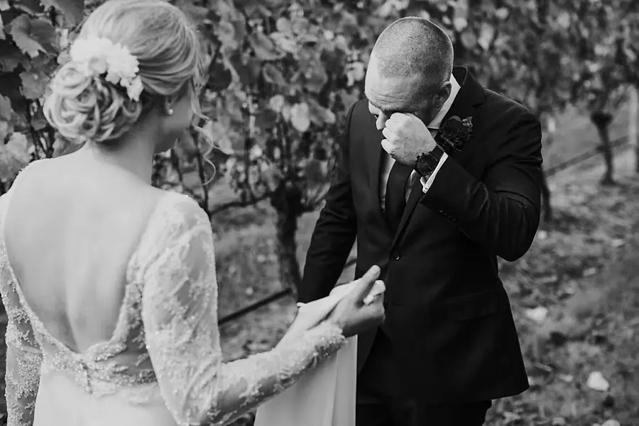 Black-and-white photograph of the groom wiping his face as he sees the bride.