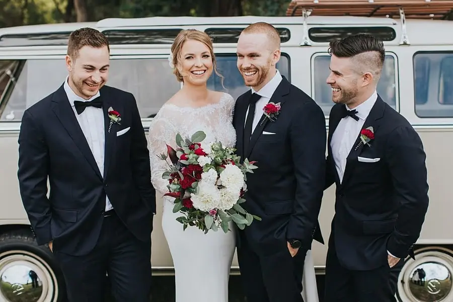 Bride posing with three men in dark suits beside the vintage van.
