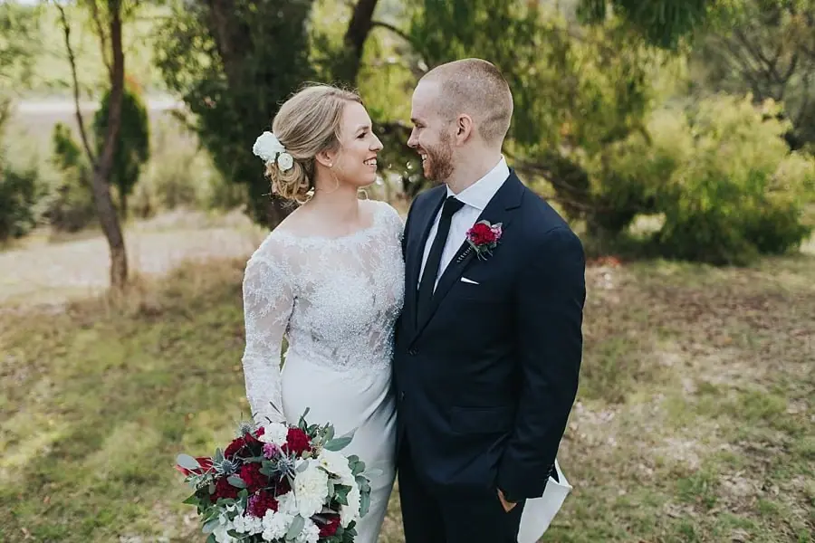 Couple smiling at each other beneath garden trees.