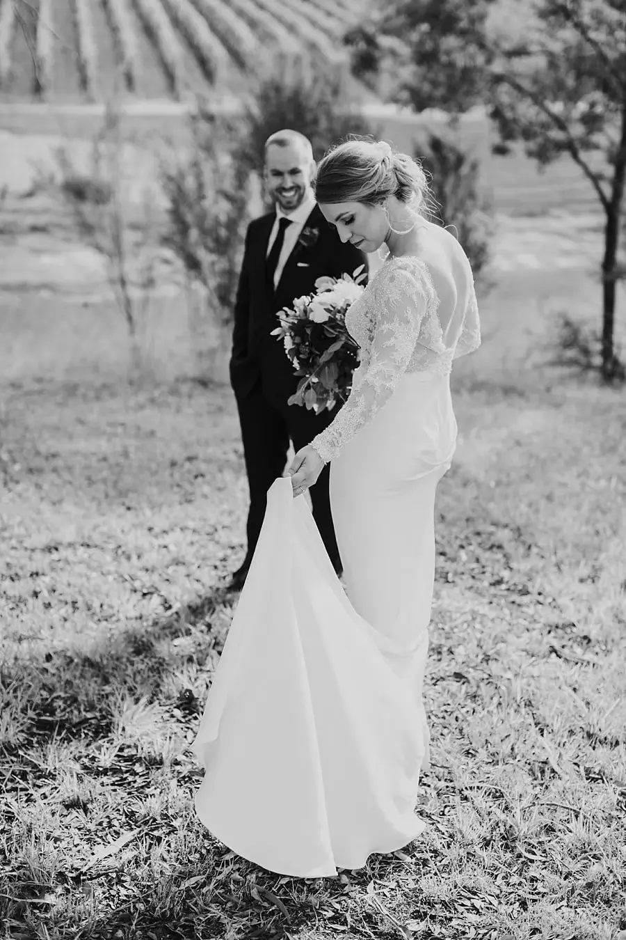 Black-and-white photograph of the bride looking down at her dress beside the groom.