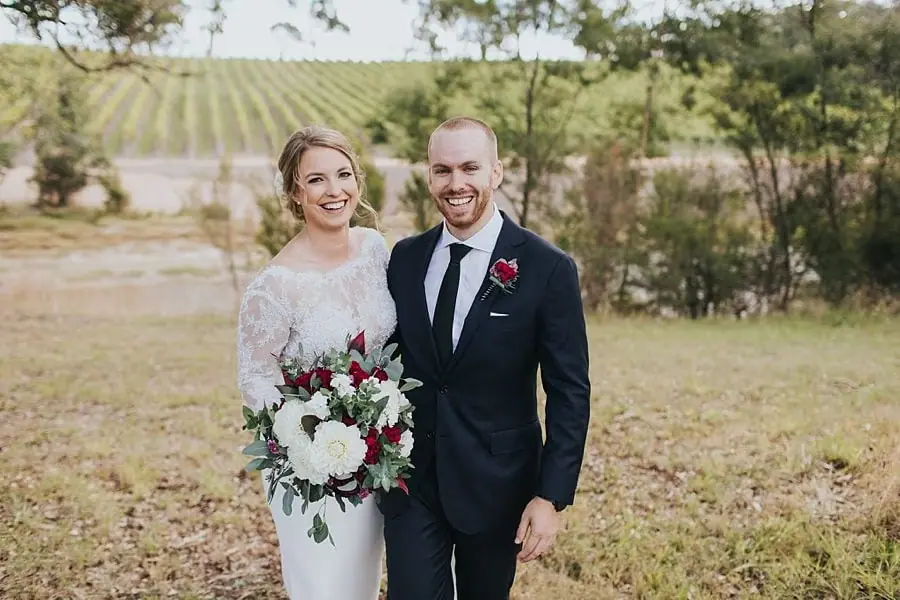 Bride and groom smiling together on a grassy slope.