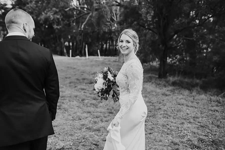 Black-and-white photograph of the bride looking back at the groom with her bouquet.