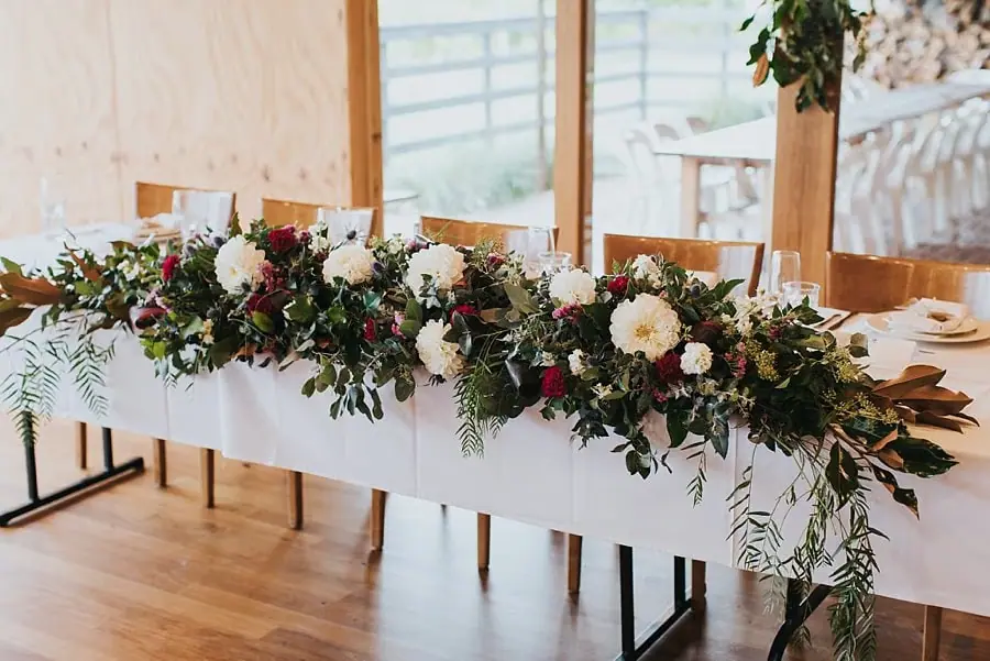 White reception table covered with red and white flowers and trailing greenery.
