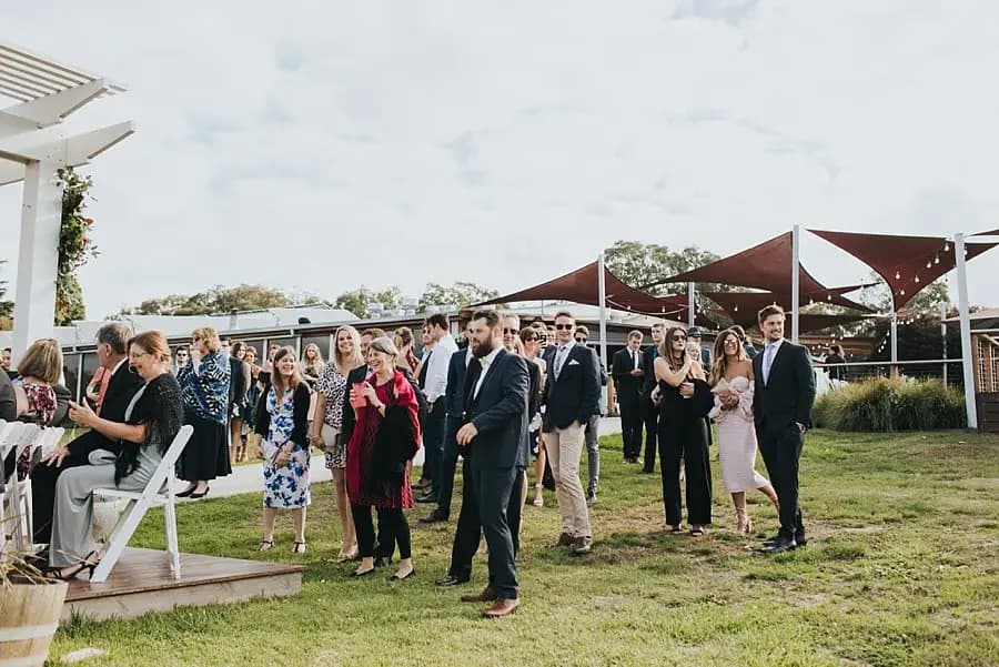 Guests standing near the outdoor ceremony beneath triangular shade sails.