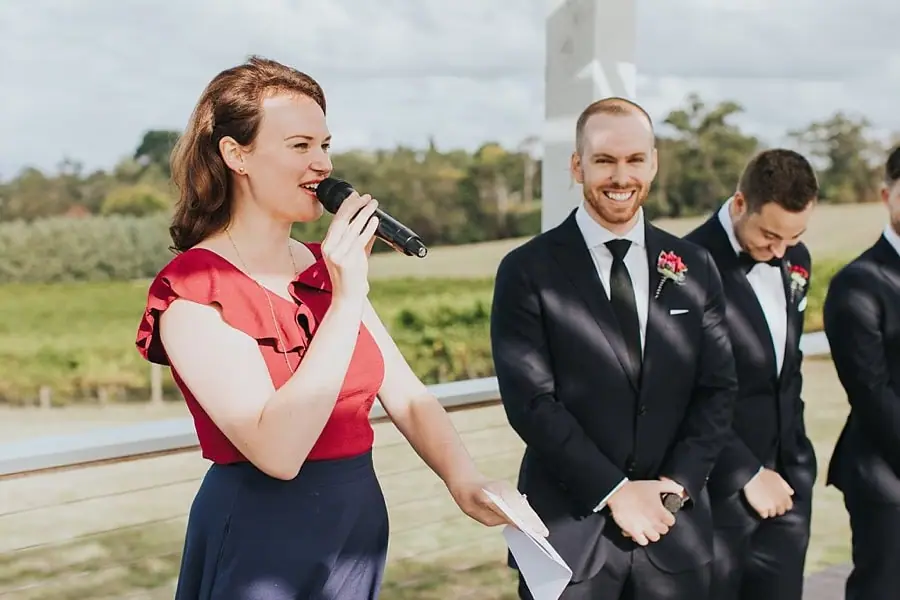 Celebrant speaking into a microphone beside the smiling groom.