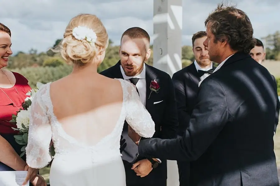 Bride and groom meeting beside a man at the front of the outdoor ceremony.