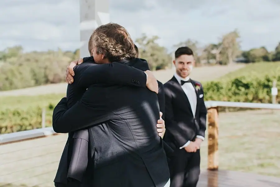 Groom embracing a man beside the ceremony pergola.