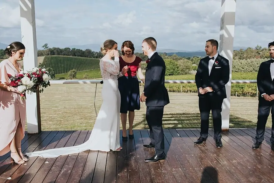 Bride and groom facing one another beside the celebrant under the white pergola.