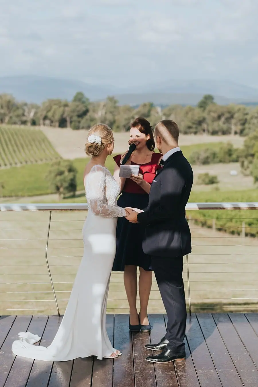Couple holding hands beside the celebrant on the wooden ceremony deck.