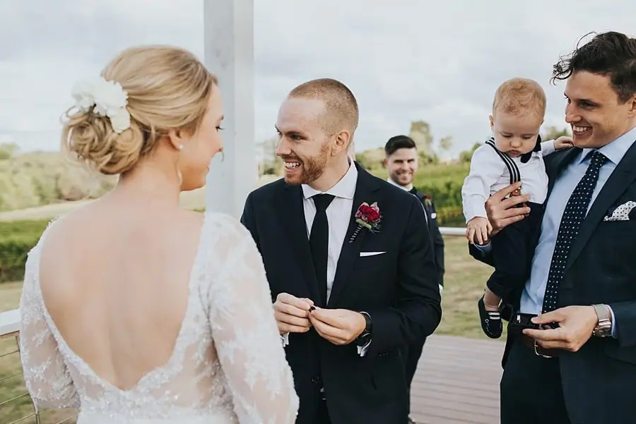 Groom smiling at the bride beside a man holding a small child.