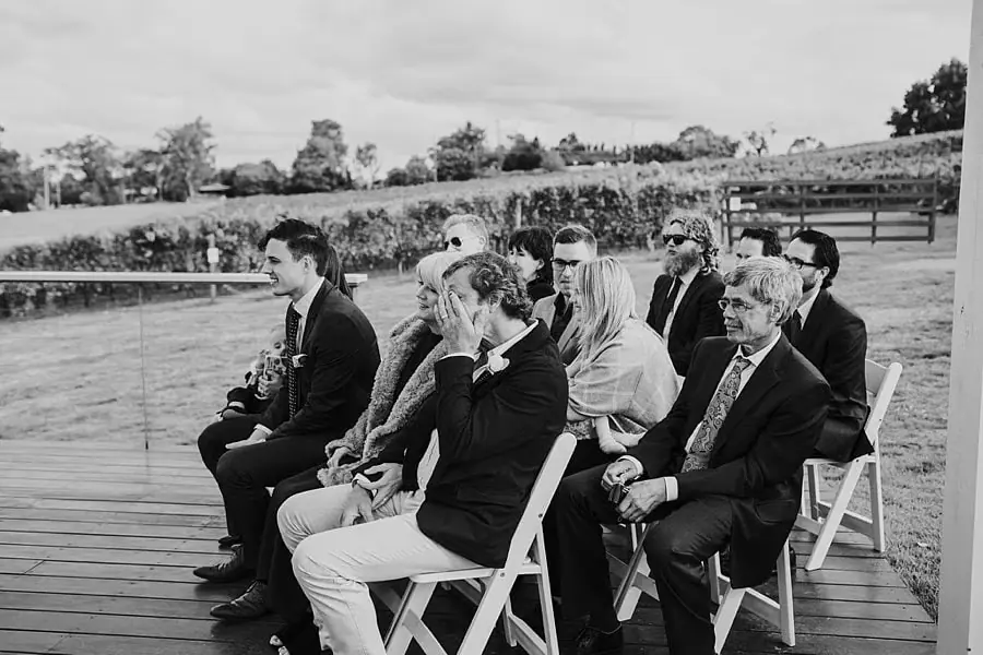 Black-and-white photograph of guests seated in rows on the wooden ceremony deck.