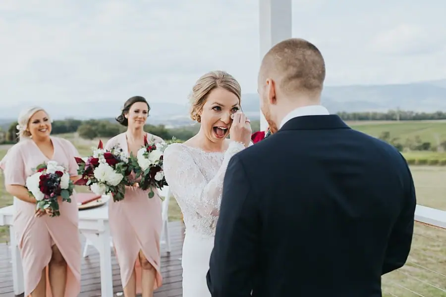 Bride making a delighted expression at the groom with bridesmaids behind her.