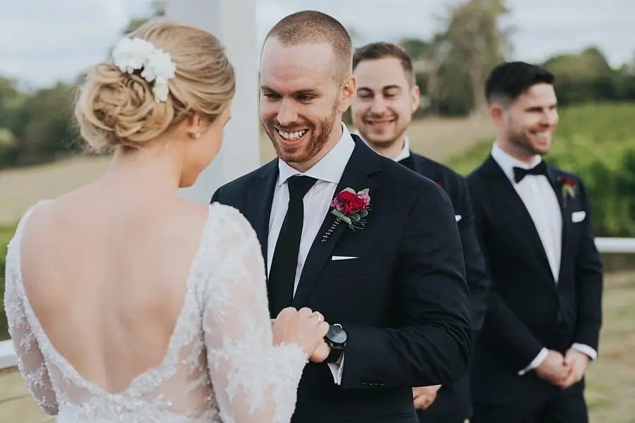 Groom smiling at the bride as their wedding party watches.