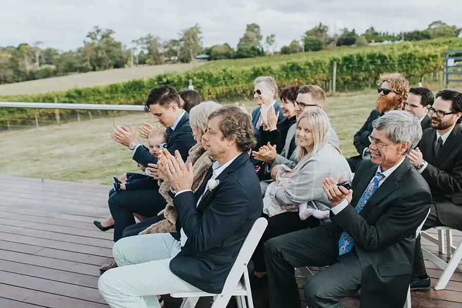 Guests applauding from white chairs on the ceremony deck.