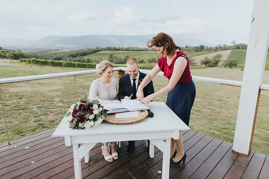 Bride and groom signing paperwork at a white table beside the celebrant.