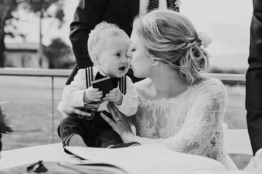 Black-and-white photograph of the bride kissing a smiling small child.