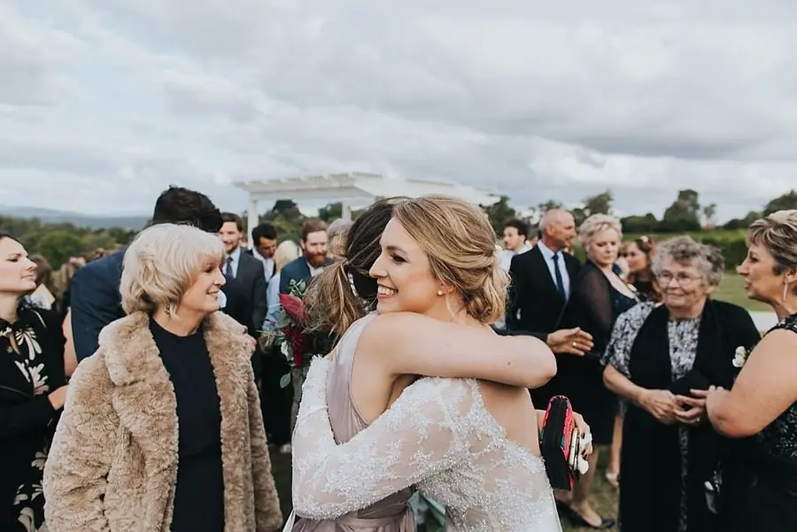 Bride embracing a guest among people gathered outside.