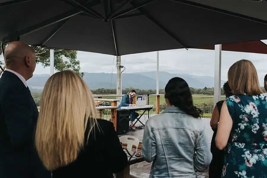 Guests gathered beneath patio umbrellas while a keyboard musician performs.