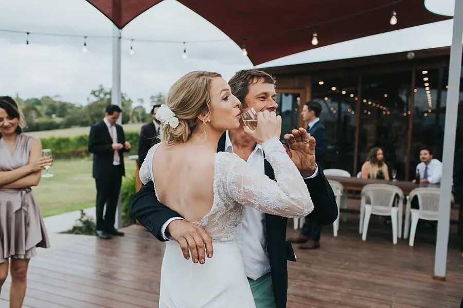Bride embracing a man on the deck beneath string lights.