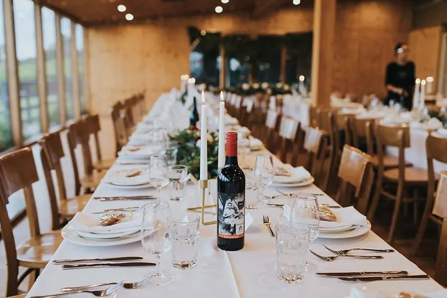 Wine bottles, glassware and place settings along a white reception table.