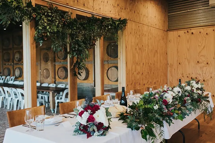 Floral reception table beneath hanging greenery against timber walls.