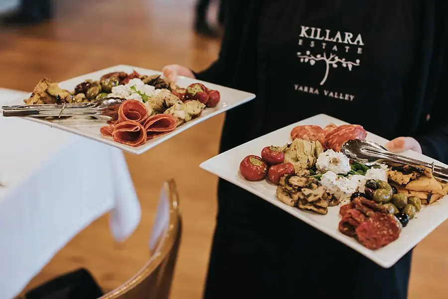 Server holding two platters of sliced meats and vegetables.