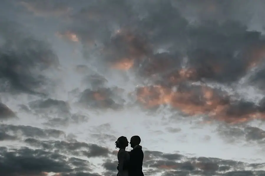 Couple silhouetted against dramatic sunset clouds.