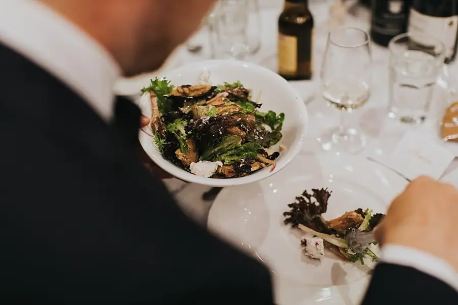 Guest holding a plate of food above a reception table.