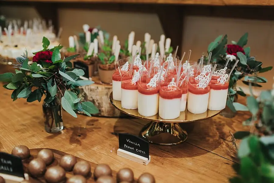 Small dessert glasses topped with red sauce and spoons beside eucalyptus leaves.