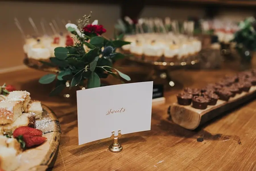 Dessert display with small cakes, fruit and a white table sign.