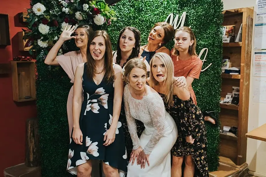 Bride and guests posing together in front of a green floral photo backdrop.