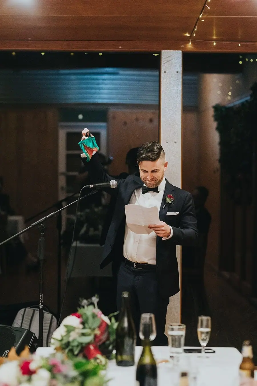 Man reading notes into a microphone in front of the reception windows.