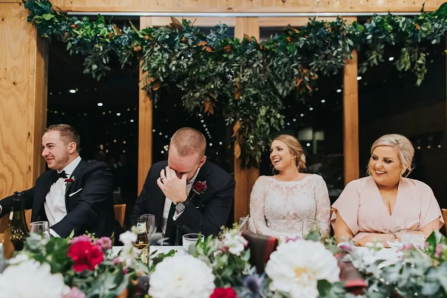 Bride laughing as the groom covers his face at the head table.