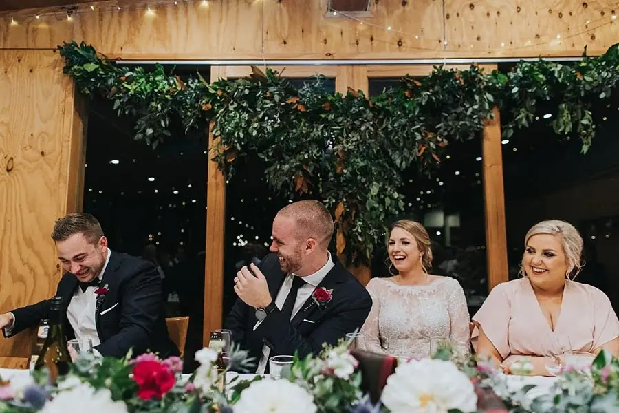 Groom and companions laughing together behind the reception flowers.