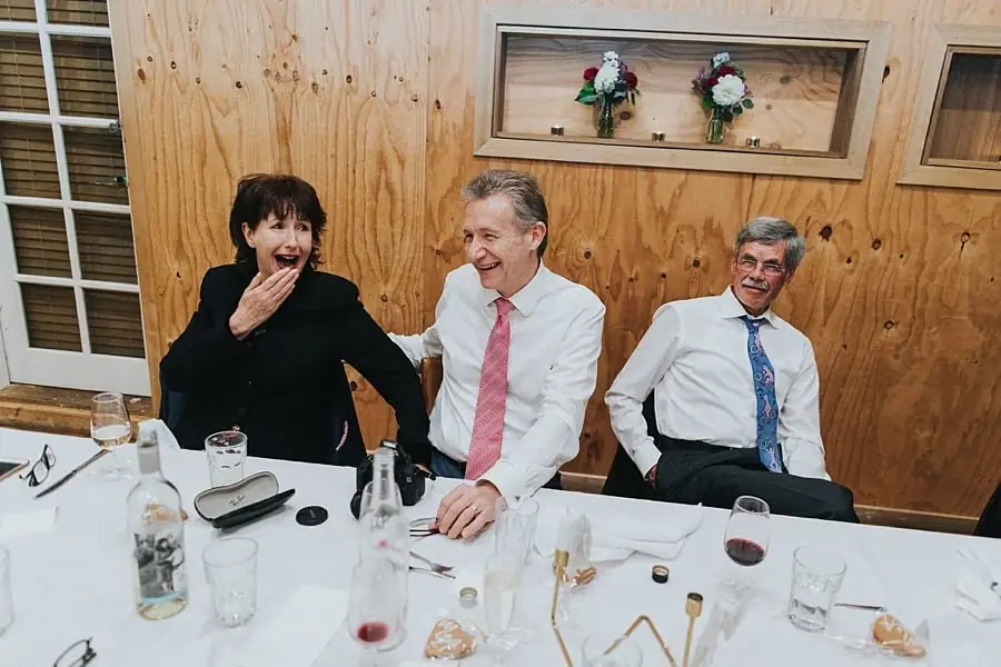 Three guests laughing together in front of a timber wall.