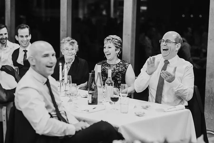 Black-and-white photograph of guests laughing and applauding around a table.