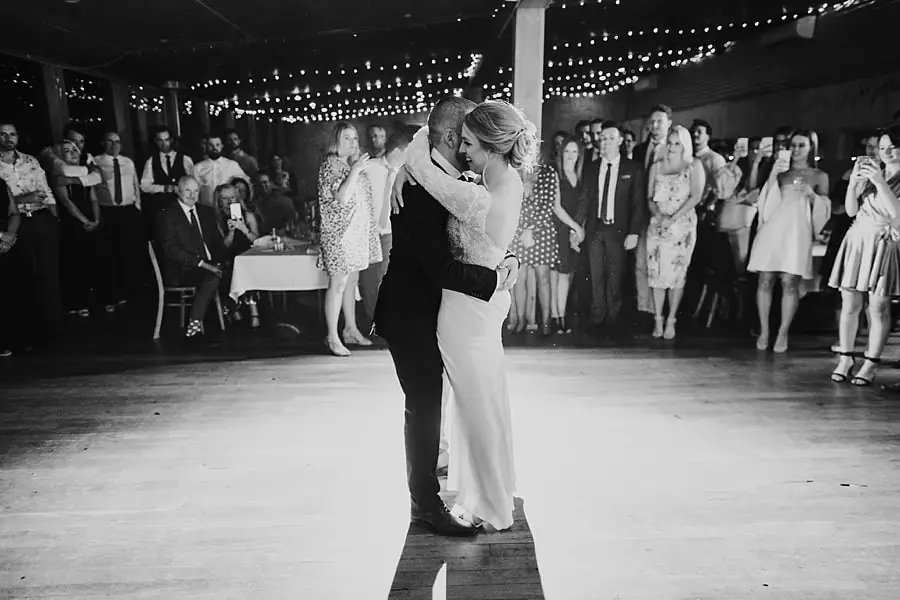 Black-and-white photograph of the couple kissing on the dance floor while guests watch.