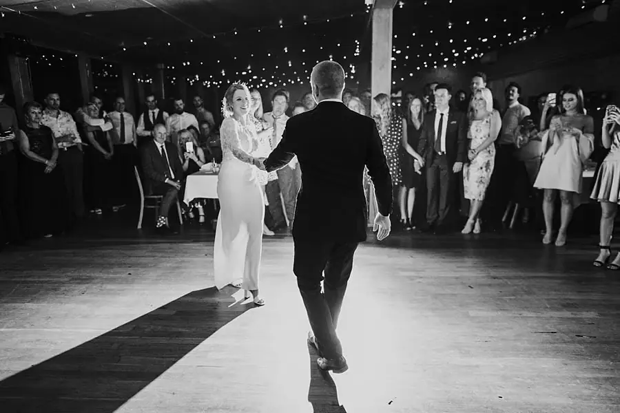 Black-and-white photograph of the bride and groom holding hands across the dance floor.