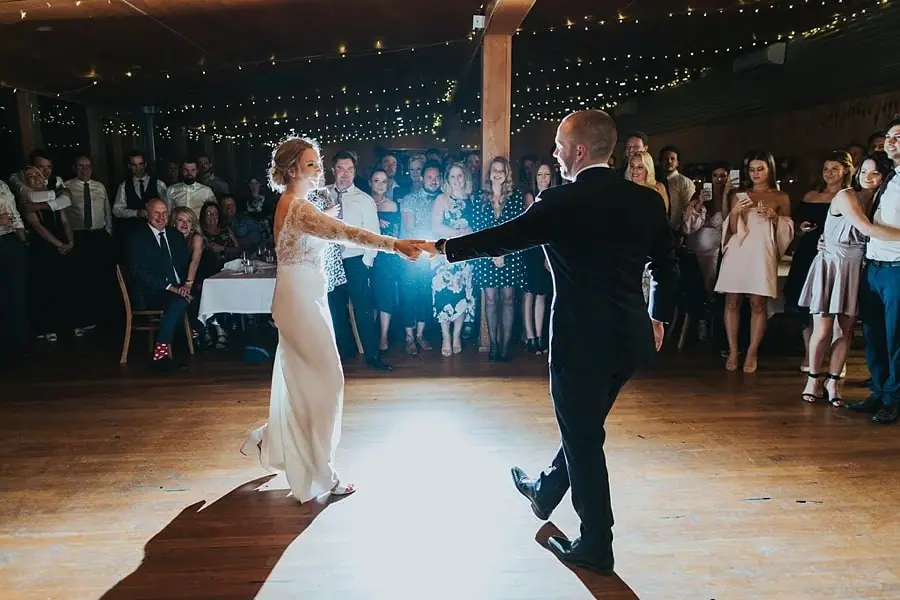 Bride and groom holding hands and dancing beneath reception lights.