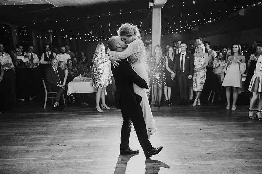 Black-and-white photograph of the groom lifting the bride in an embrace on the dance floor.