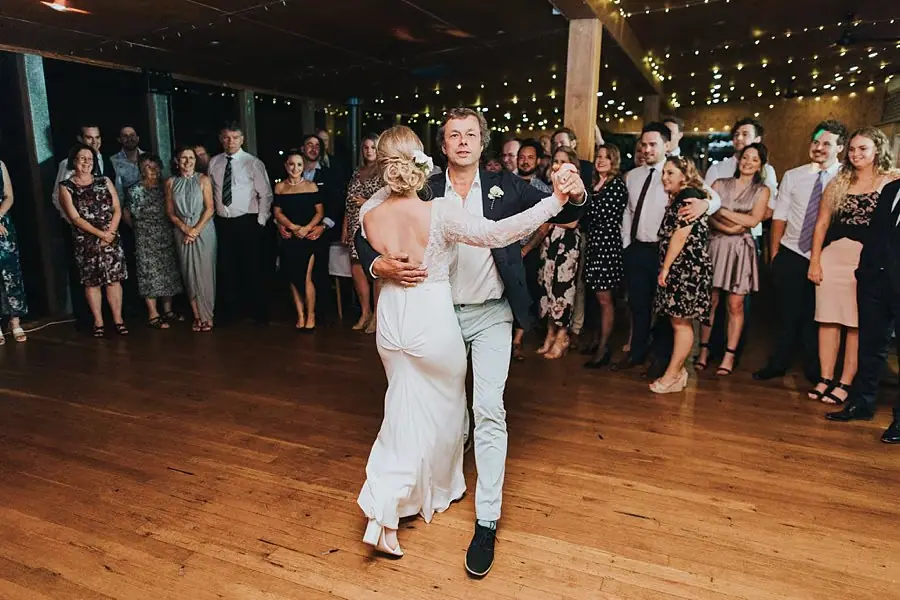 Bride dancing with a man in a dark jacket and pale trousers.