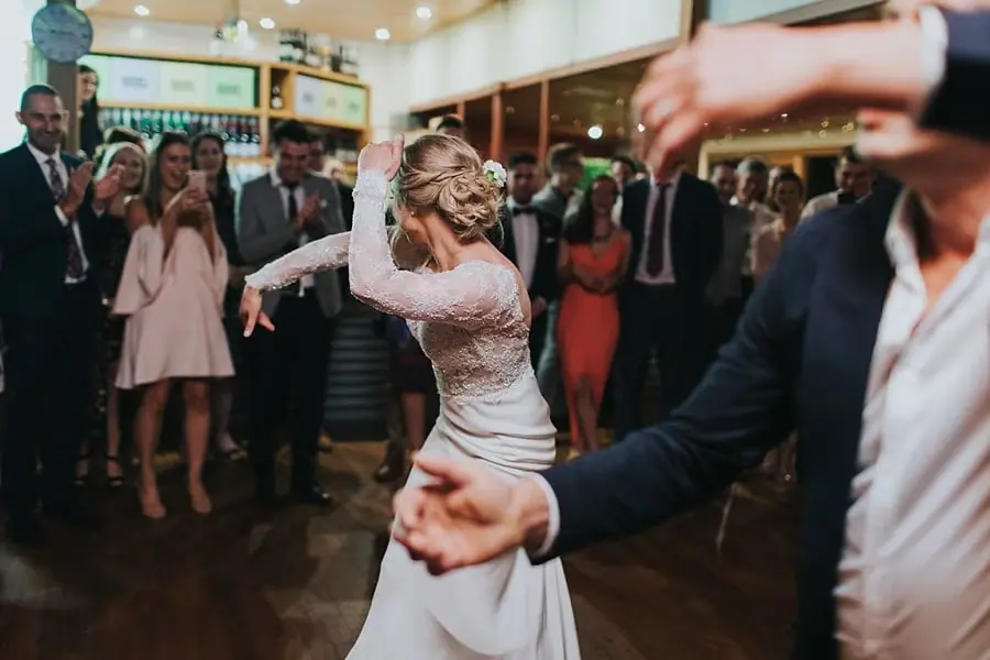 Bride raising her arms and dancing among guests.