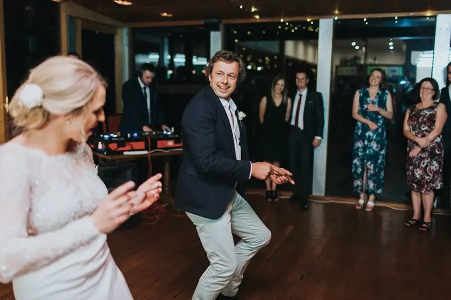 Man dancing and smiling toward the bride on the reception floor.