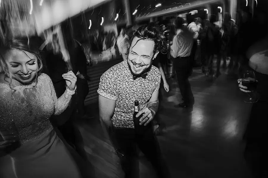 Black-and-white photograph of two guests smiling and dancing beneath streaks of light.